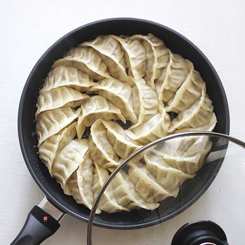 フライパンで羽根つき餃子を焼いている途中の写真。蓋を開け、羽根が色づき始めた状態